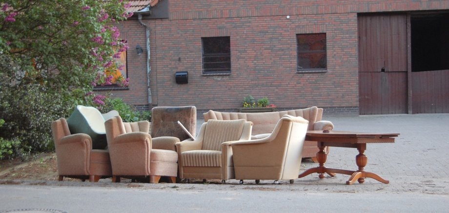 Ein alter Tisch, ein Sessel und eine Couch stehen als Sperrmüll vor einem Bauernhaus